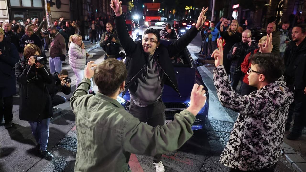 Young people dance and raise their arms in a Belgrade street on Sunday evening, Oct. 25, 2026, after Aleksandar Vučić conceded Serbia’s parliamentary election, as a photographer records the scene