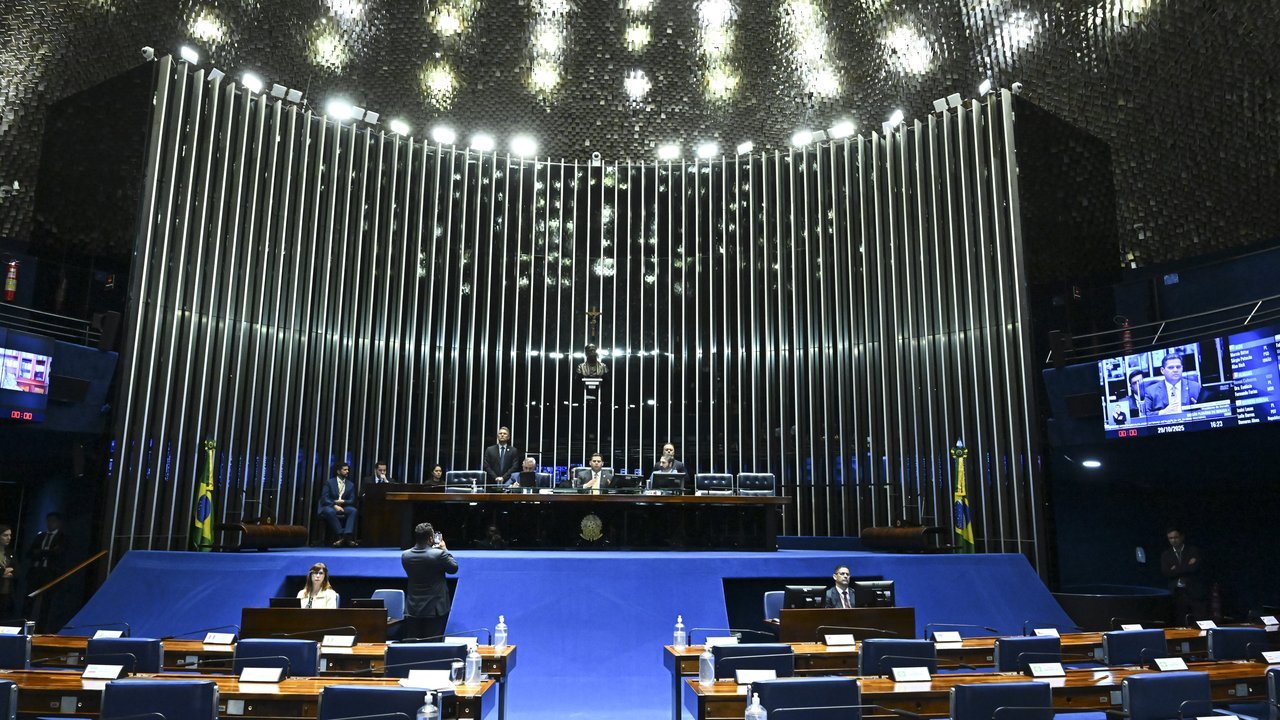 Stand-in, not a photo of this event: the plenary chamber of Brazil’s Federal Senate in Brasília during an October 29, 2025 session, with blue carpet, rows of wooden desks, officials at the raised head table and a wall of vertical metal slats under a lit, textured ceiling