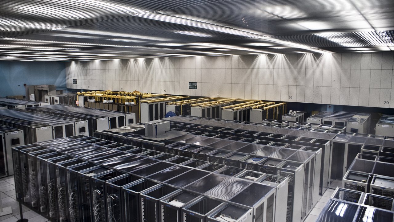 Stand-in, not a photo of this event: rows of grey and silver server racks with mesh doors fill a large, brightly lit server room at CERN in Switzerland in February 2009, under a ridged metal ceiling, with yellow cable trays over the racks in the middle distance