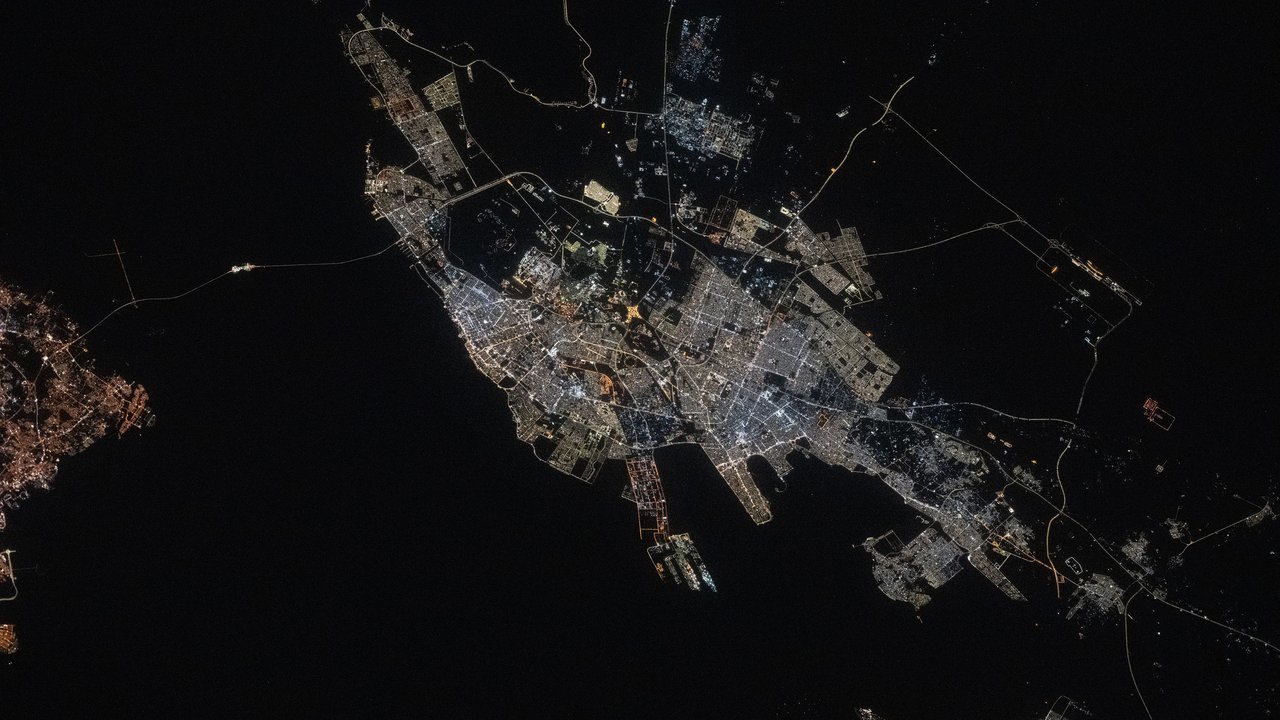 Stand-in, not a photo of this event: Dammam at night, seen from the International Space Station on May 22, 2025, with white and amber city lights and a port pier spread along the dark Persian Gulf coast; the photo predates the attack