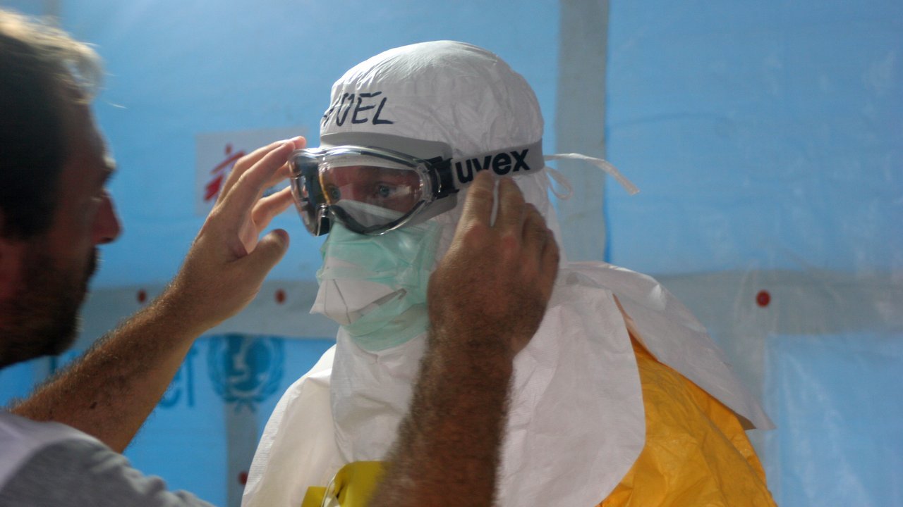 Archival stand-in: a health worker in protective gear adjusts a colleague’s goggles before he enters an Ebola treatment unit in Liberia, August 2014