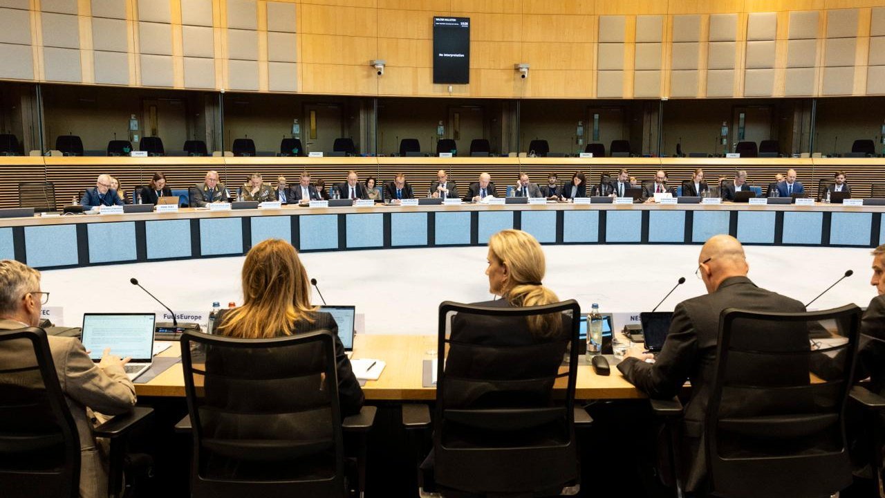 Photo posted on X by @Energy4Europe: seen from behind, several delegates sit at a curved conference table in a wood-panelled European Commission meeting room, facing a long row of officials and industry representatives across an open floor, with name cards and microphones on the desks