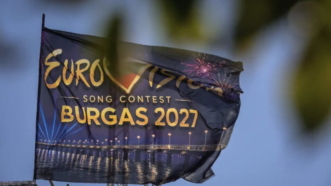 Photo posted on X by @unidosxisrael: a dark blue flag reading “Eurovision Song Contest Burgas 2027” over a lit pier at night with fireworks, blowing in the wind behind blurred leaves