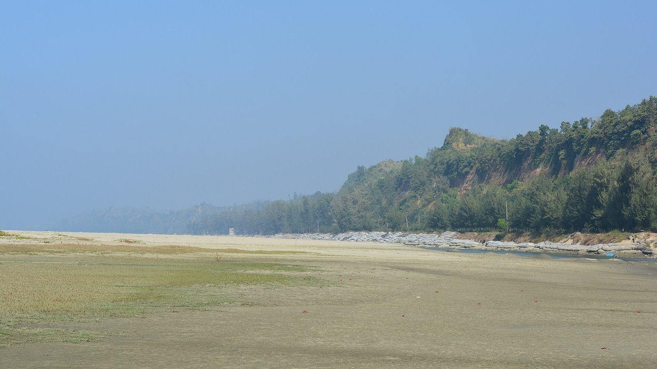 Stand-in, not a photo of this event: February 2017 file photo of Inani Beach in Cox’s Bazar, a wide, flat stretch of sand under a hazy blue sky, with forested hills along the shore and a line of grey rocks at the water’s edge