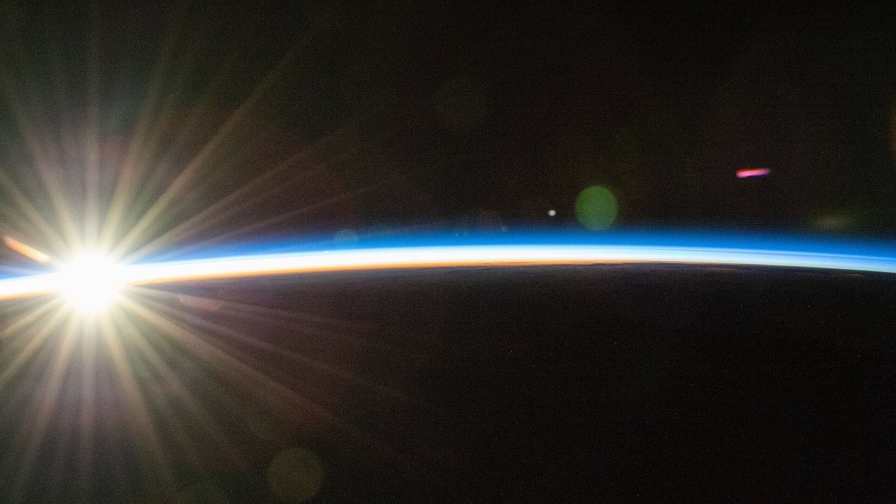 Illustration: an orbital sunrise bursts over Earth’s curved horizon, lighting thin bands of atmosphere, photographed from the International Space Station in November 2025