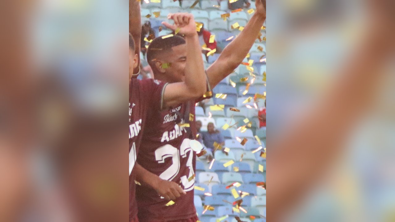 Jayden Adams, wearing a maroon Stellenbosch FC shirt with ADAMS and the number 23, raises his arms among falling gold confetti at the December 2023 Carling Knockout trophy celebration