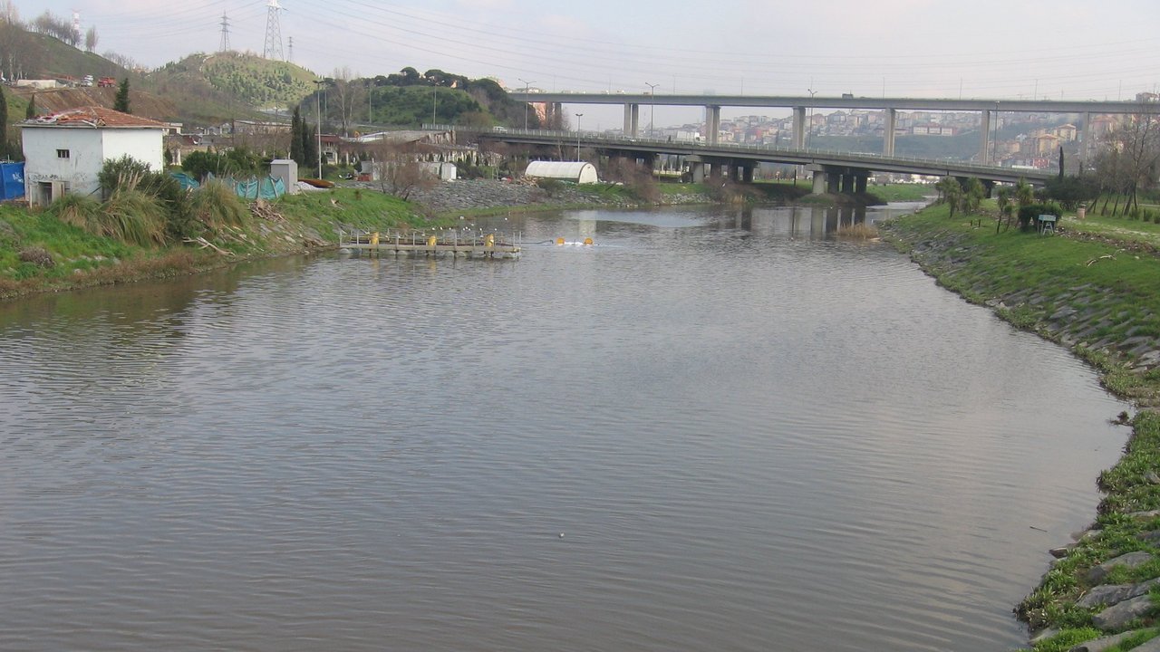 Stand-in, not a photo of this event: 2009 view of the calm Kağıthane stream in Istanbul between grassy, stone-lined banks, with a highway viaduct and hillside buildings behind