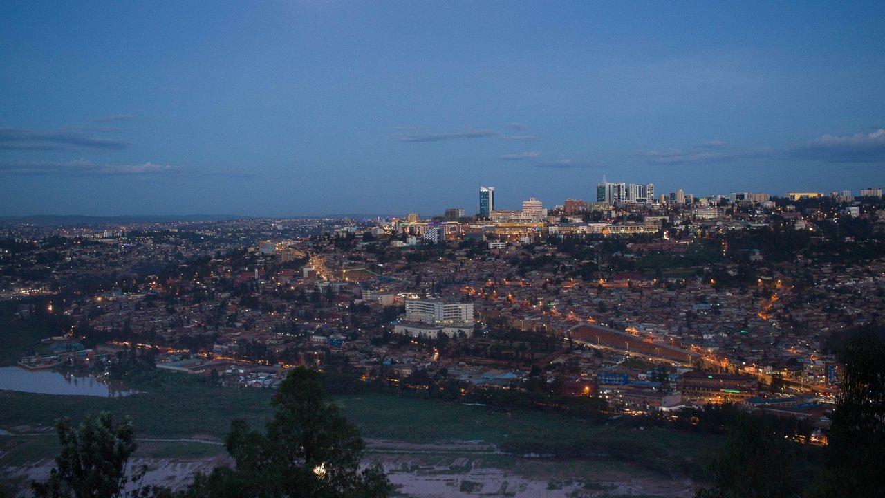 Stand-in, not a photo of this event: a May 2018 file photo of central Kigali at dusk, with lit high-rise towers on a ridge above hillside neighbourhoods and a stretch of water and trees in the foreground
