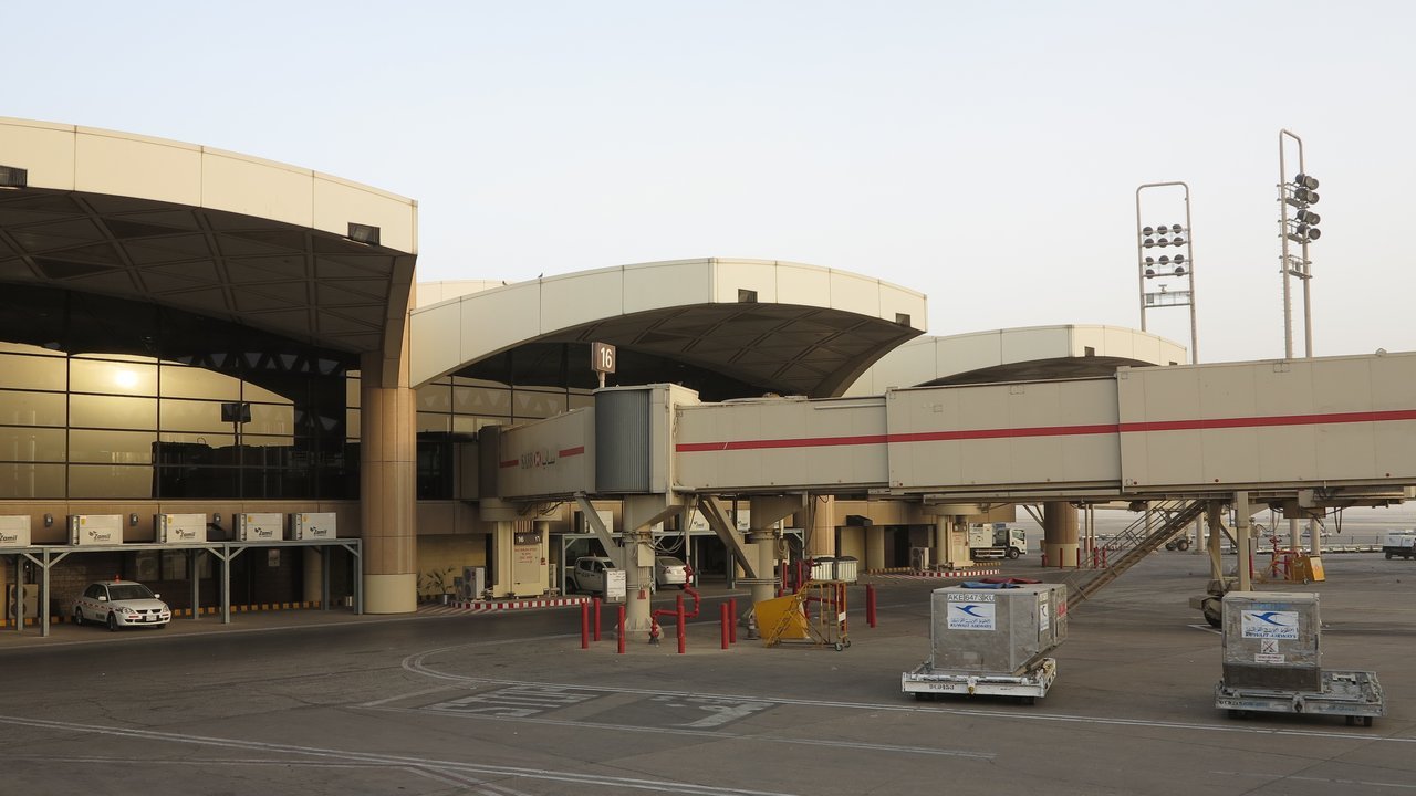 Stand-in, not a photo of this event: a March 2013 file photo of the curved terminal buildings and jet bridges at King Khalid International Airport in Riyadh, with cargo containers and a parked car on the apron