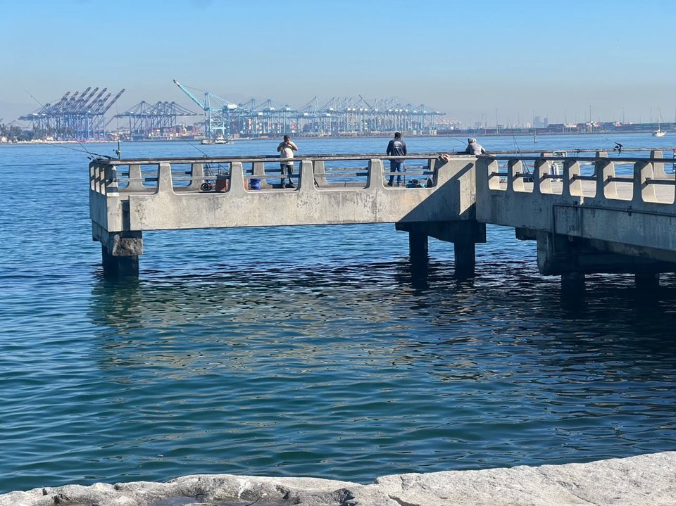 Photo posted on X by @ConwayShow: calm, high water reaches close to the deck of the Cabrillo Beach pier in San Pedro on Oct. 26, 2026, with a few people fishing on the pier and Port of Los Angeles cranes on the horizon