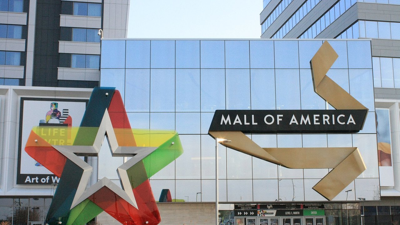 Stand-in, not a photo of this week: the front entrance of the Mall of America in Bloomington, Minnesota, with its glass facade, its name sign, and a large multicolored star sculpture, in an April 2021 photo
