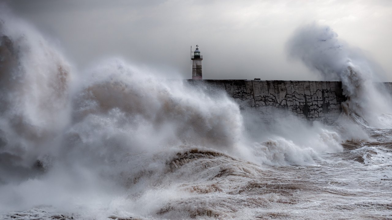 Stand-in, not a photo of this event: huge grey waves explode over the breakwater and small lighthouse at Newhaven, East Sussex, under a low storm sky, in a 2023 photo