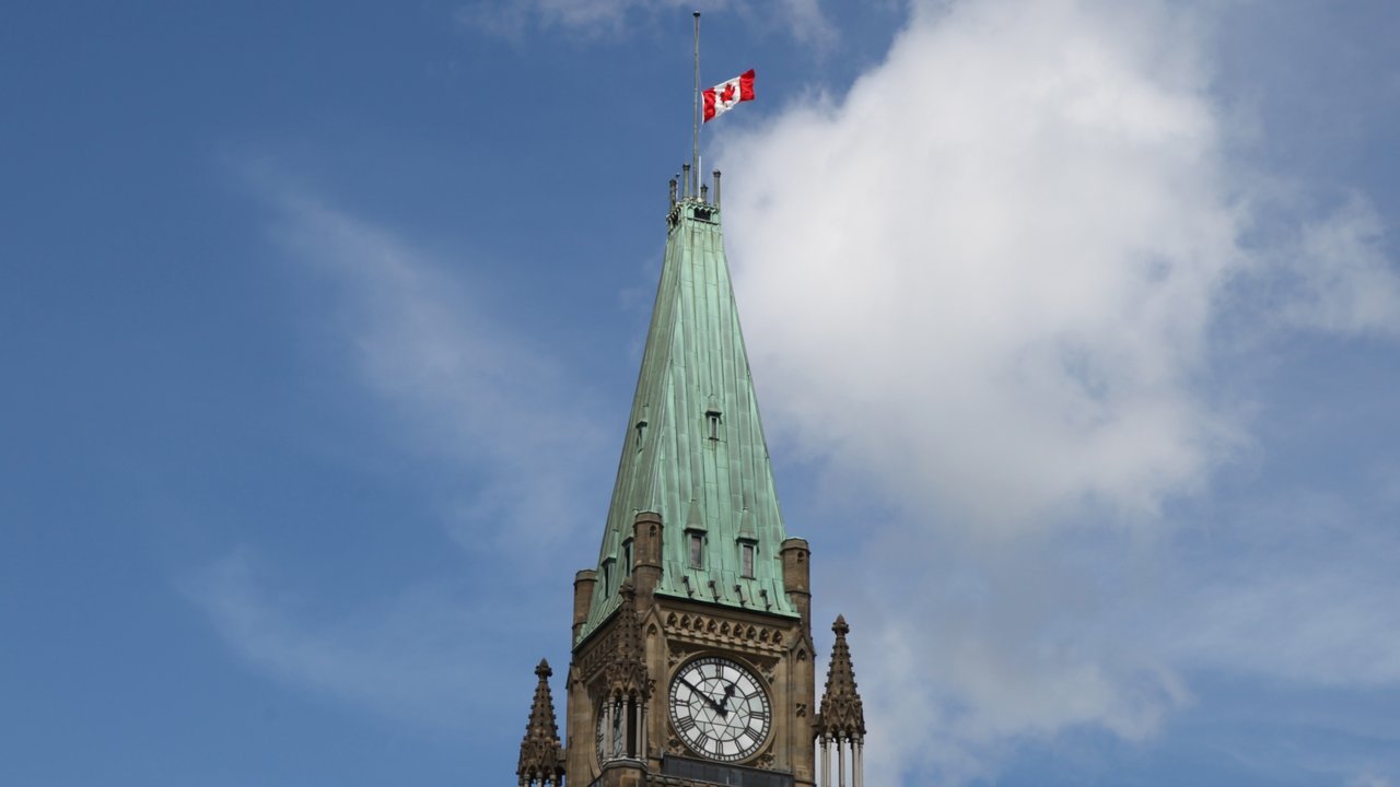Stand-in, not a photo of this event: August 2011 file photo of the Canadian flag at half-mast atop the Peace Tower in Ottawa, with its green copper roof and clock face under a blue sky