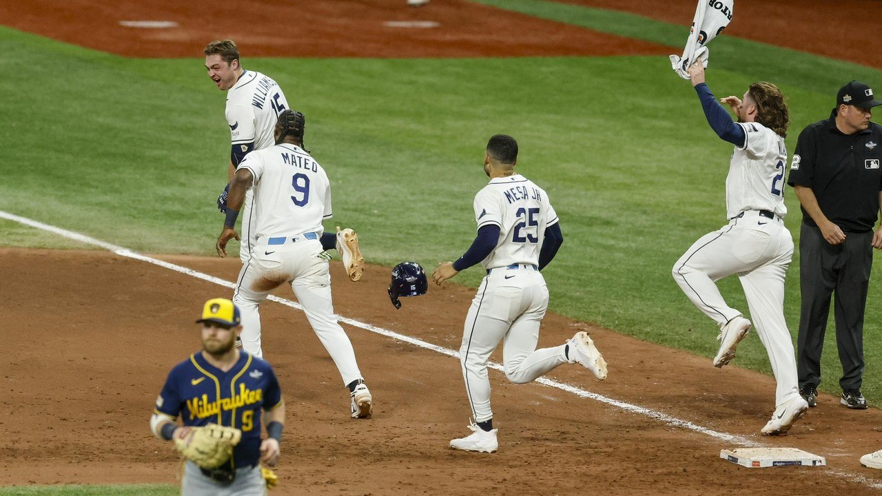 Photo posted on X by @RaysBaseball: Tampa Bay Rays players in white home uniforms run and leap along the first-base line at Tropicana Field after the winning hit in Game 4 of the World Series, one waving a towel, as a Milwaukee Brewers infielder in a navy jersey walks off in the foreground and an umpire watches