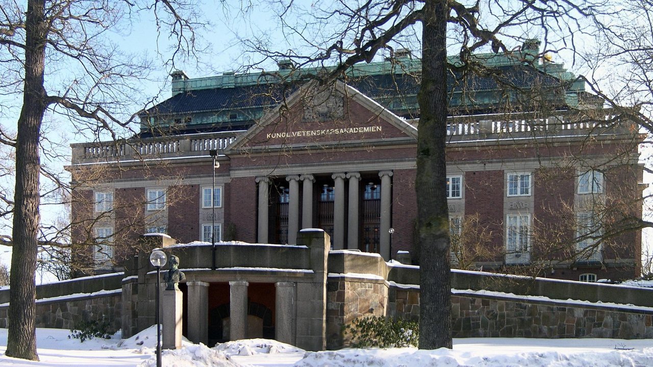 Stand-in, not a photo of the announcement: a 2006 file photo of the red-brick main building of the Royal Swedish Academy of Sciences in Stockholm, with columns, a pediment reading Kungl. Vetenskapsakademien, bare trees and snow in front