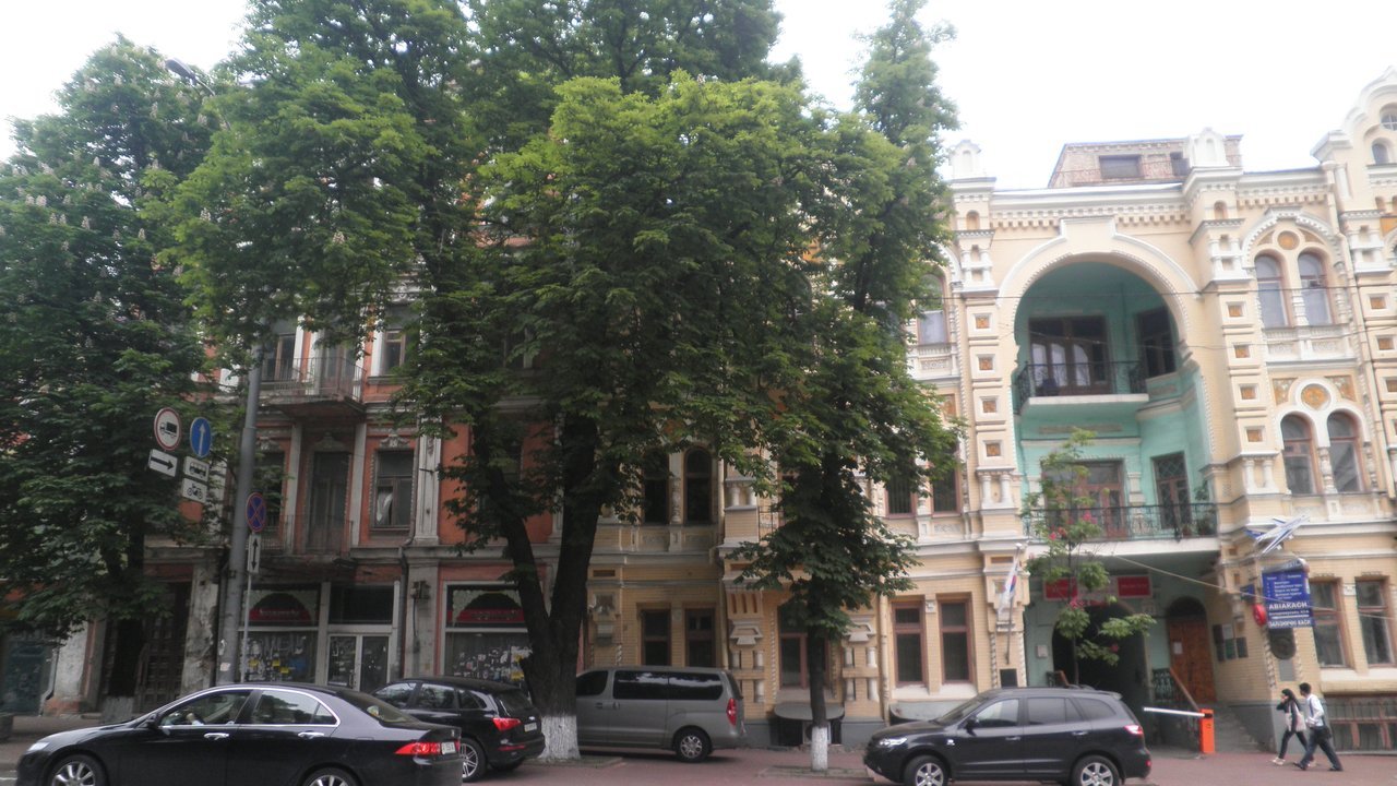 Stand-in, not a photo of this event: a Kyiv street of ornate, cream and terracotta 19th-century-style buildings behind tall leafy trees, with cars parked at the curb, in a 2012 photo its uploader titled the Embassy of the Republic of Korea in Kyiv