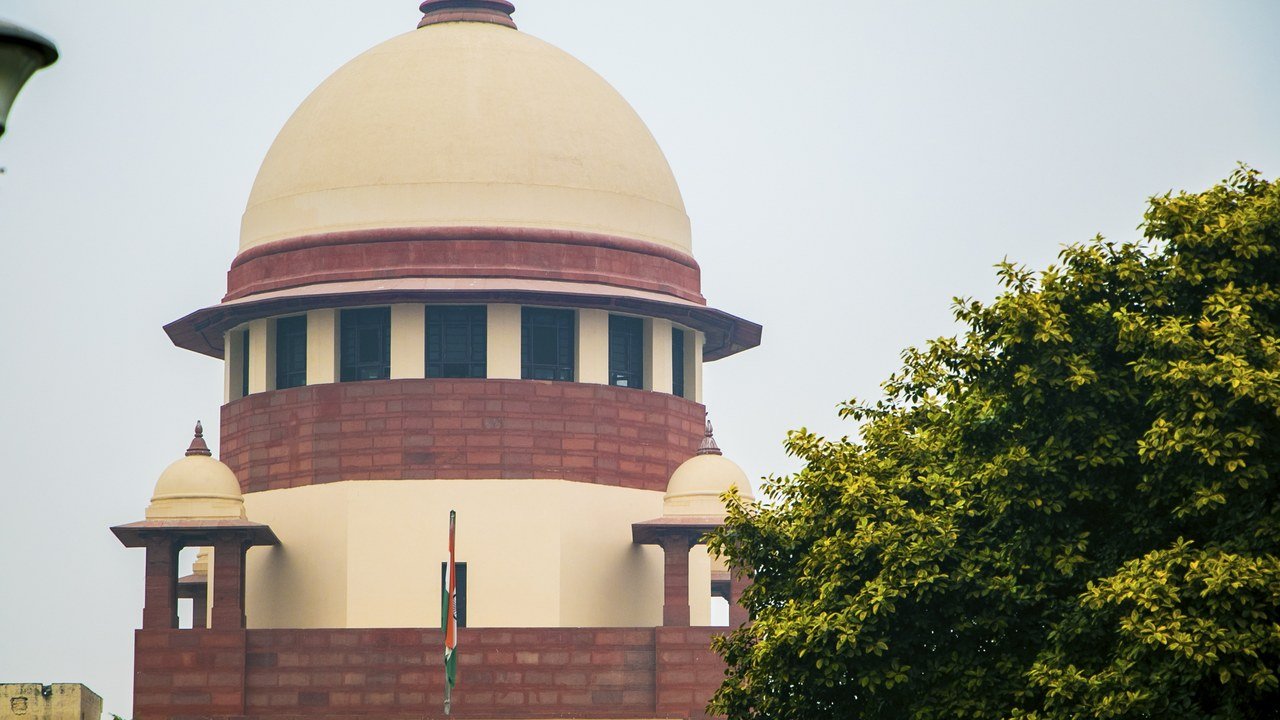 Stand-in, not a photo of this event: a December 2019 file photo of the cream dome and red sandstone central wing of the Supreme Court of India in New Delhi, with the national flag on a pole in the foreground and a green tree at right
