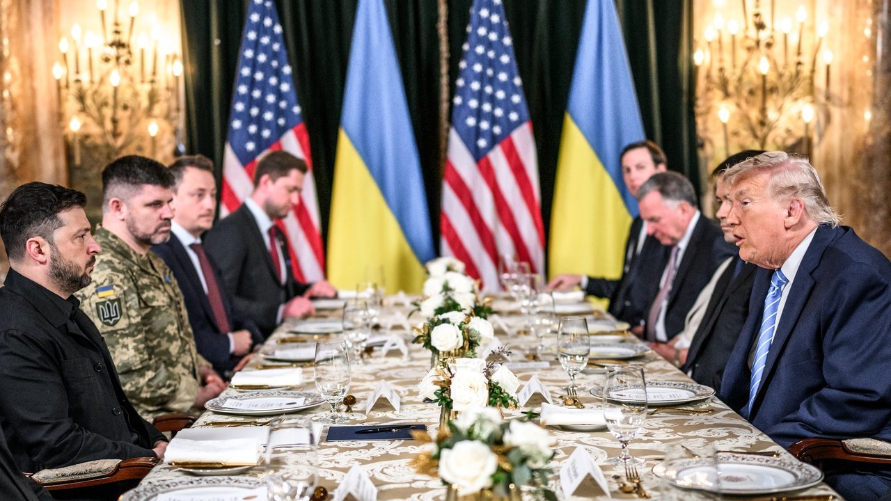 File photo, not from this week: Ukrainian President Volodymyr Zelensky and U.S. President Donald Trump sit across a long table with aides at Mar-a-Lago, with U.S. and Ukrainian flags behind them, December 28, 2025