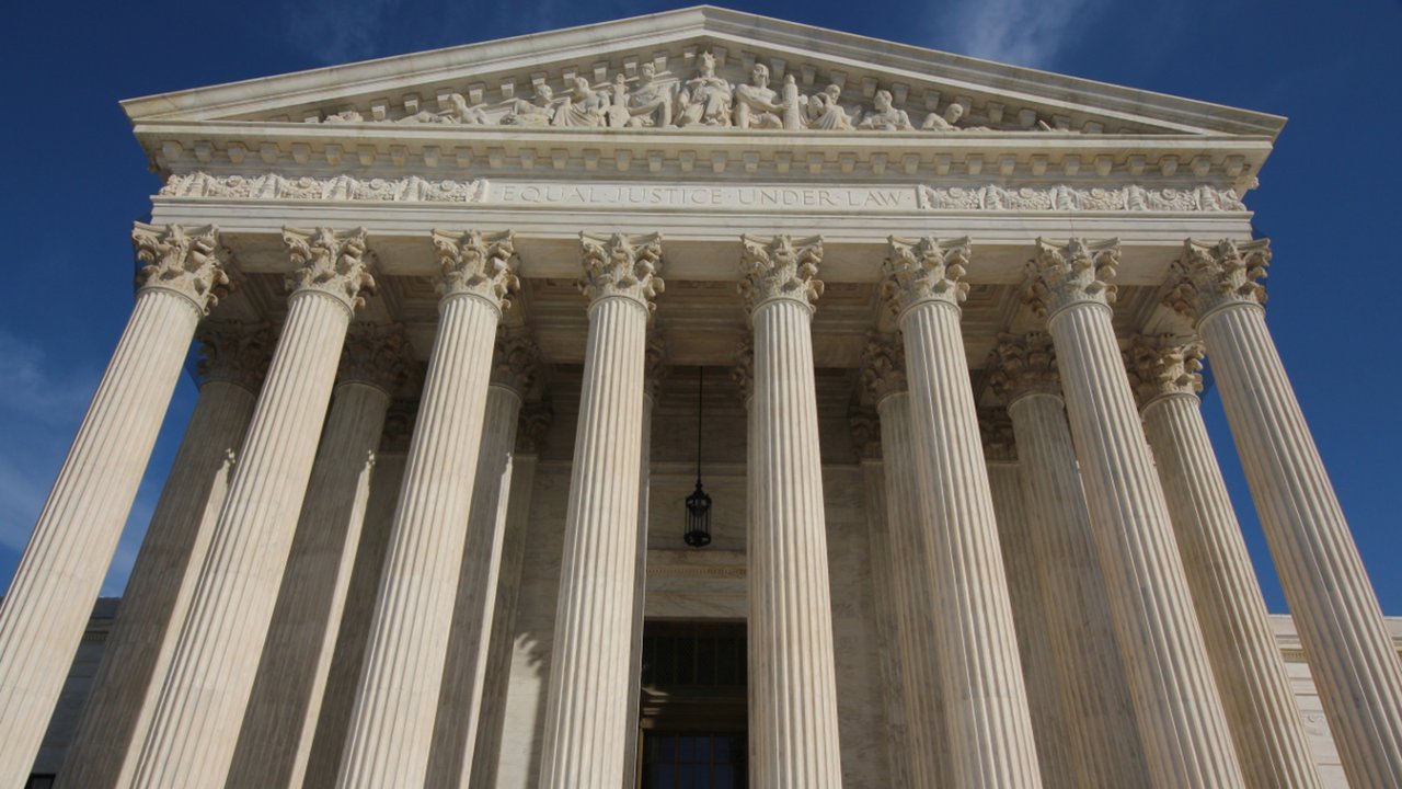 Stand-in, not a photo of this event: the west front of the U.S. Supreme Court Building in Washington, seen from below against a deep blue sky, with tall white Corinthian columns, a carved pediment and the frieze words Equal Justice Under Law